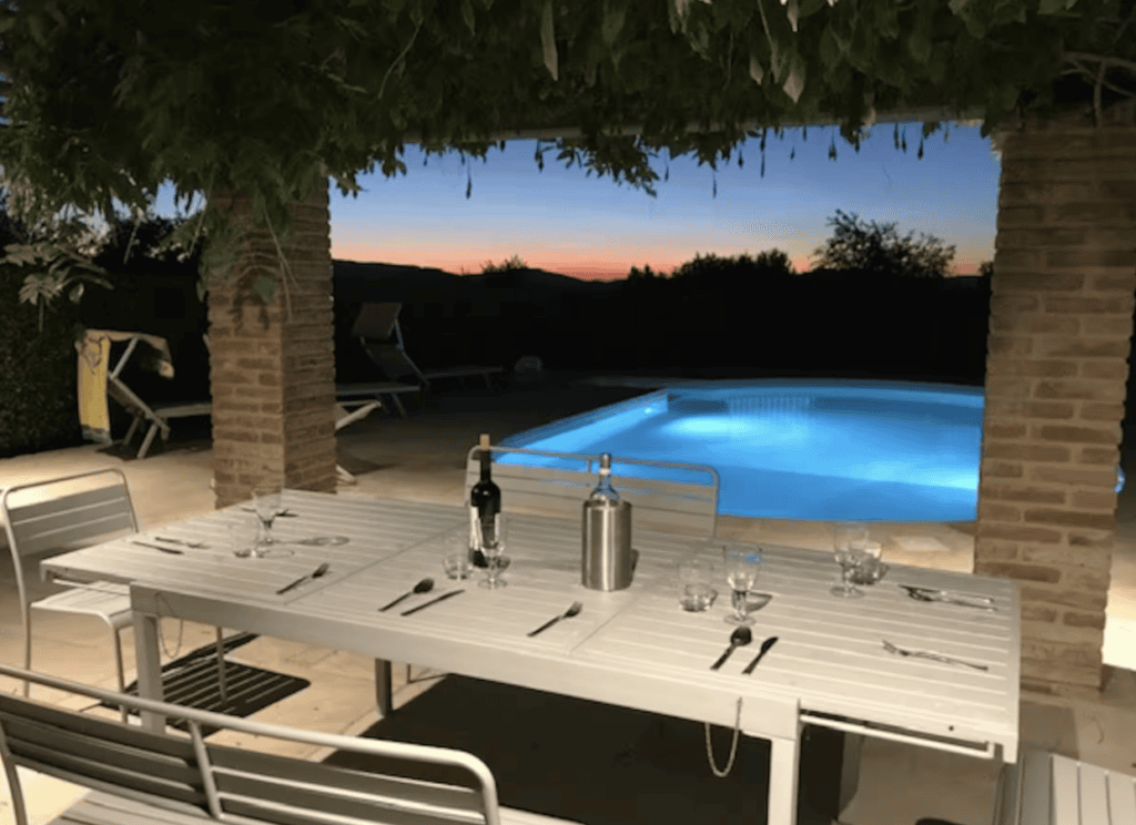 Outdoor dining terrace overlooking the illuminated swimming pool at Hilltop Farmhouse, perfect for al fresco evenings in Umbria.