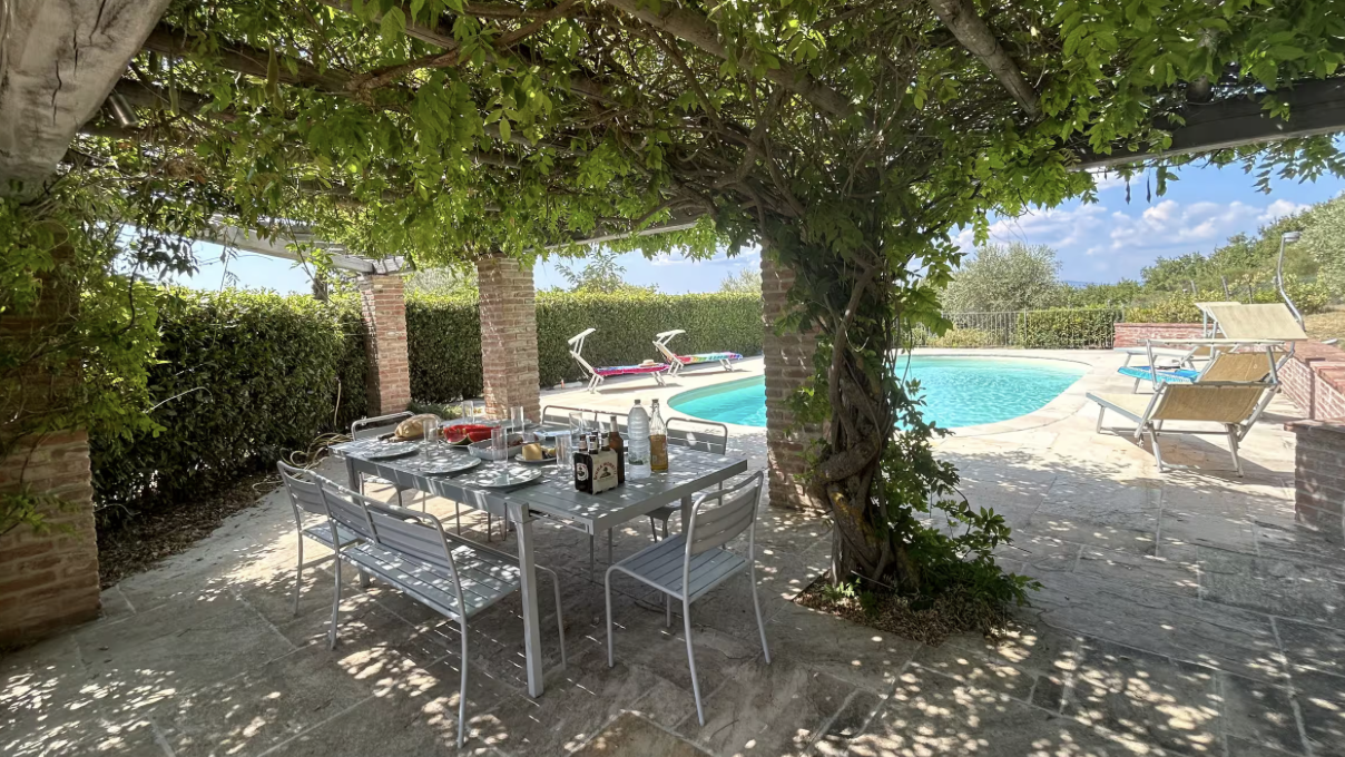 Shaded outdoor dining terrace overlooking the private swimming pool at Hilltop Farmhouse, perfect for al fresco meals in the Umbrian countryside.